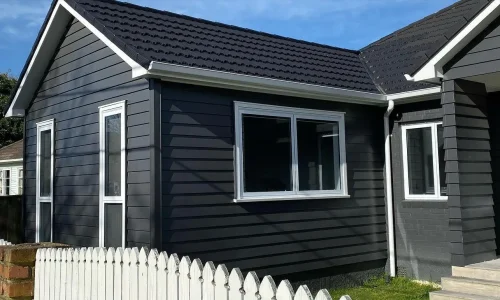 Renovated house exterior with dark siding and a white picket fence by Fencing Cromwell.